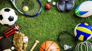 An assortment of all sports gears placed circularly on a grassy field, including a tennis racket, football, baseball gloves, etc