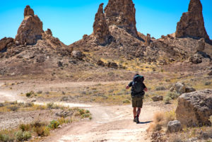 An adventurer with a backpack heads towards the Saudi mountains in summer, learn more by joining the Arab Hiking group on Hala Yalla